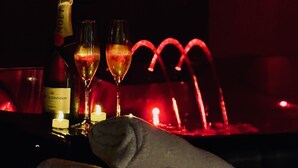 Eine schummrig beleuchtete Bar mit einer Champagnerflasche, zwei Gläsern und einer Kerze auf einer Theke.