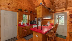 A wooden cabin kitchen with a red countertop, wooden cabinets, a microwave, and a sink.