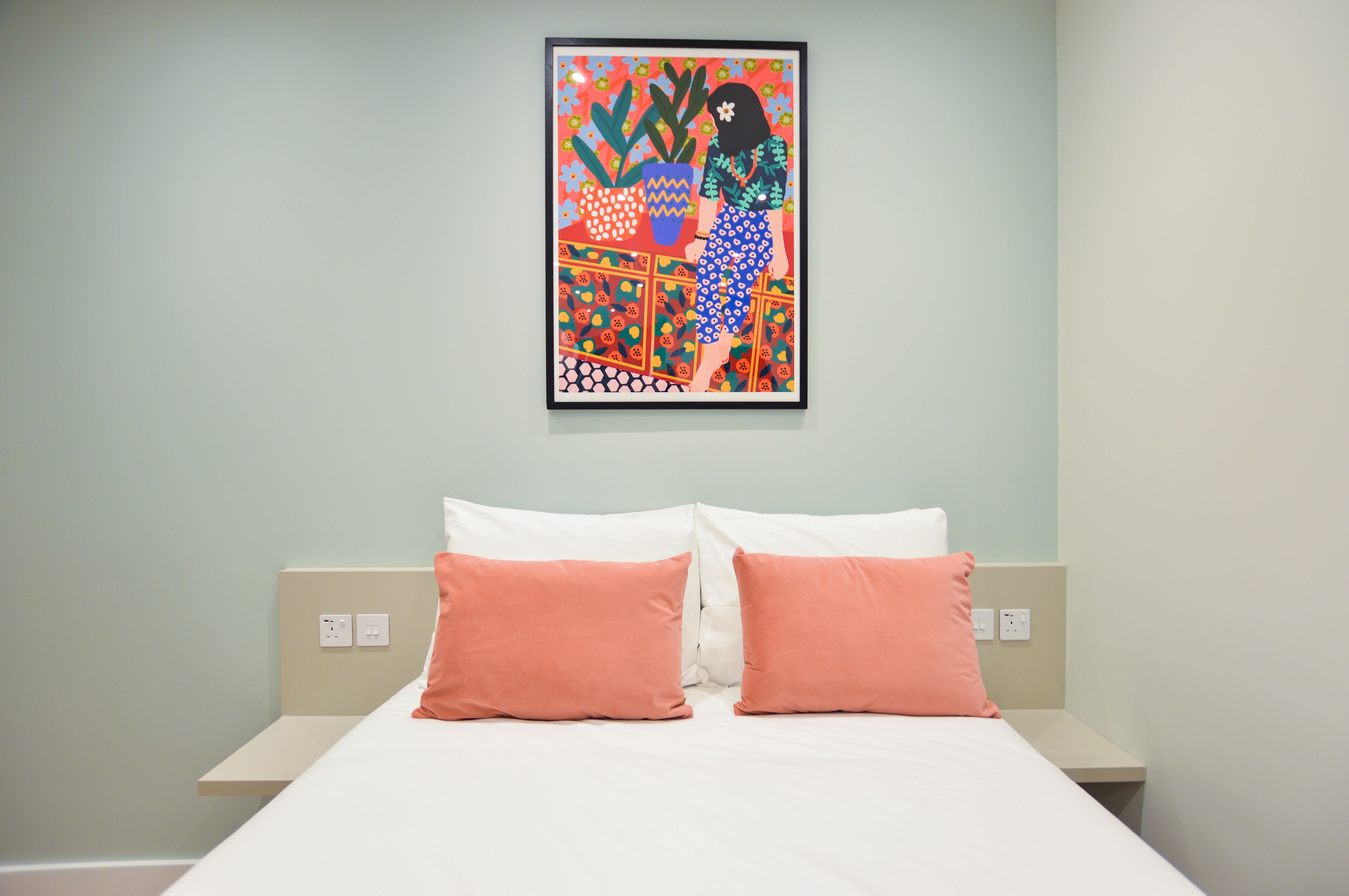 A hotel room with a bed, two pillows, a wall-mounted artwork, and a light green wall.