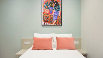 A hotel room with a bed, two pillows, a wall-mounted artwork, and a light green wall.