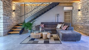 A modern living room with a stone wall, a staircase, a grey sofa, and a coffee table. - Charming Villa nestled in a region renowned for its exceptional wineries.  (Triban)