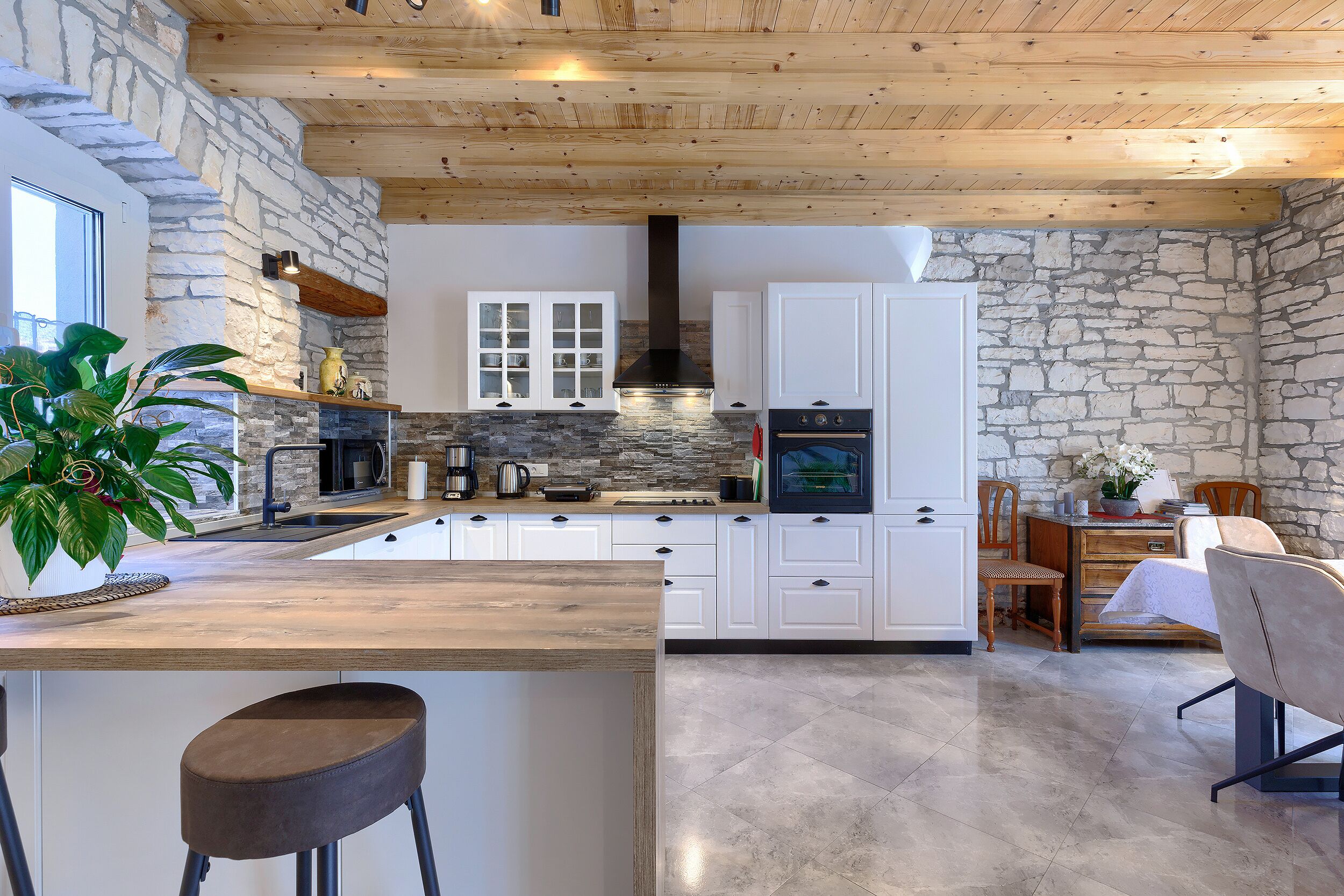 Una cocina moderna con paredes de piedra, vigas de madera en el techo y una isla central.