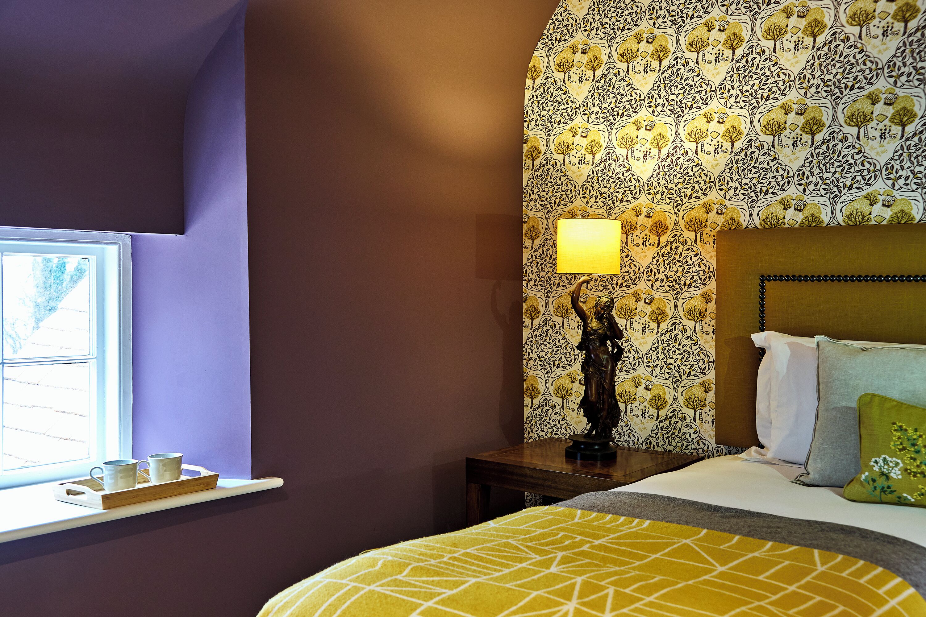 A bedroom with a bed, a nightstand, a lamp, and a window with a view.