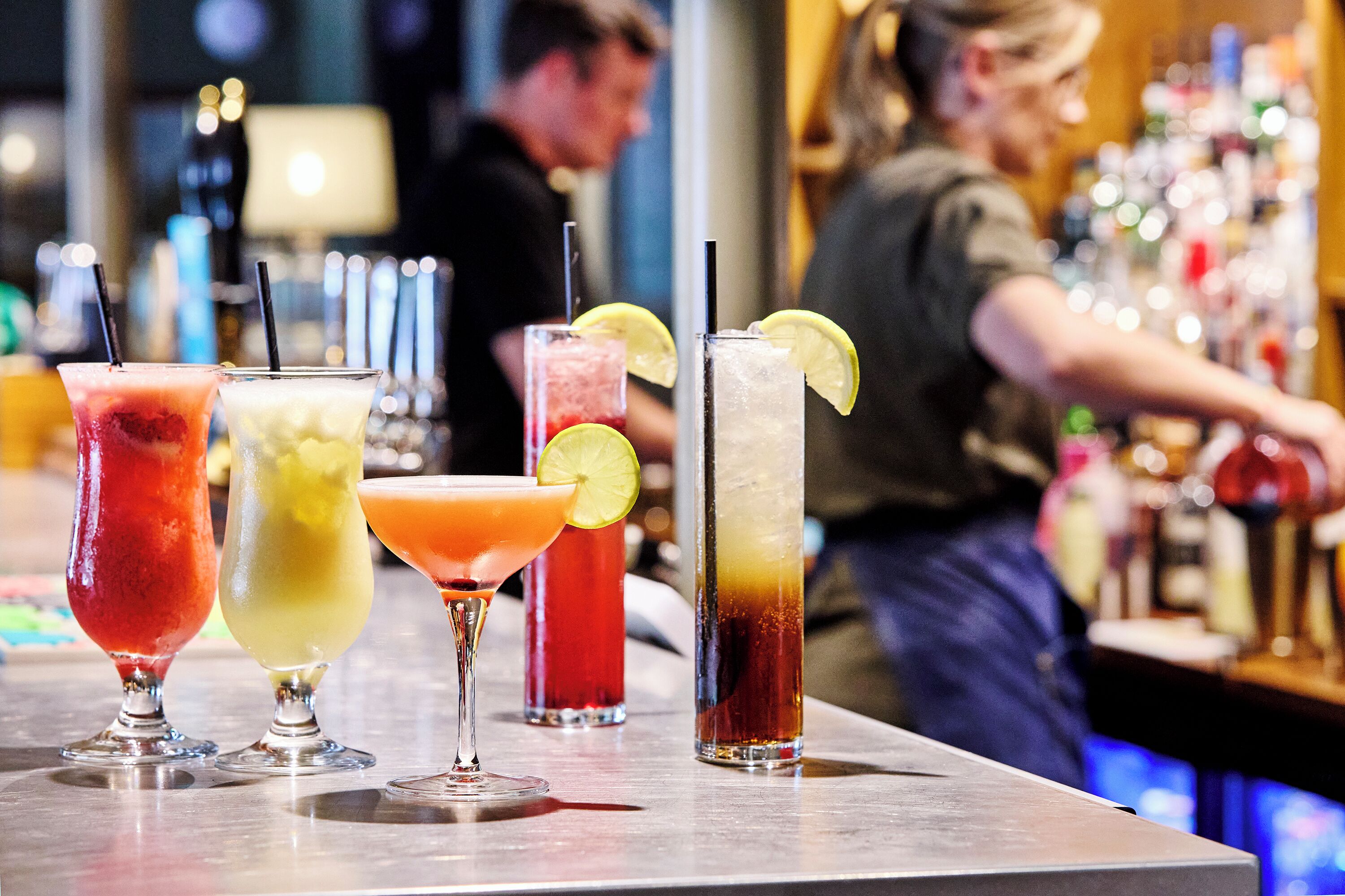 A bar with various colorful drinks, a bartender preparing drinks, and a well-stocked bar area.