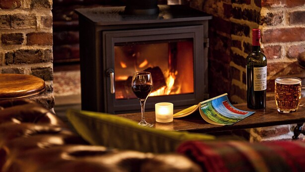 A cozy room with a brick fireplace, a wooden table with a candle, a glass of red wine, and a bottle of wine. - The Black Horse, Climping (Littlehampton)