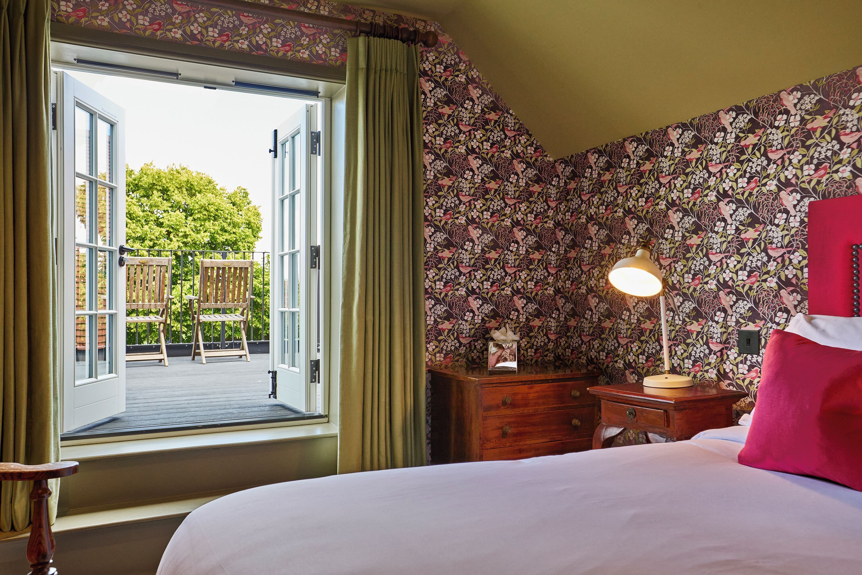 A bedroom with a bed, a nightstand, a lamp, and a window with curtains.