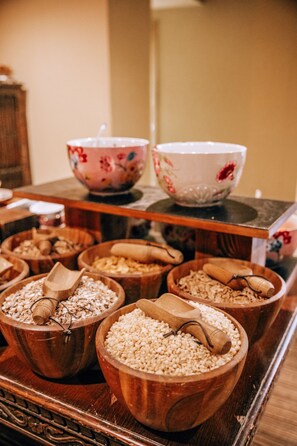 A wooden tray with various bowls containing grains and seeds, a floral-patterned bowl, and a white bowl with red flowers. - The Black Horse, Climping (Littlehampton)