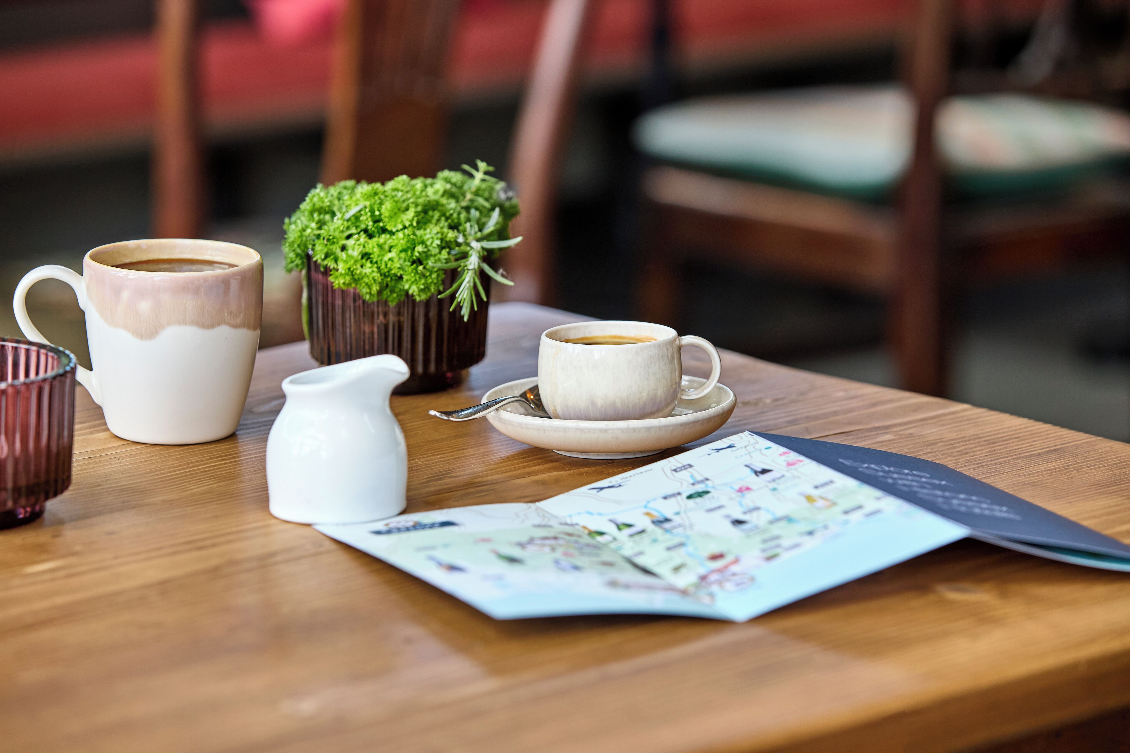 A wooden table with a white pitcher, a cup of coffee, a small potted plant, and a menu.