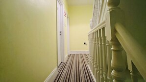A hallway with a striped carpet, a white door, and a staircase with a balustrade. - Station Hotel (Norwich)