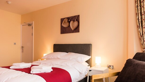 A hotel room with a bed, a bedside table, a chair, and a wall-mounted artwork. - Station Hotel (Norwich)