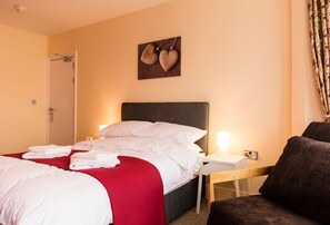 A hotel room with a bed, a bedside table, a chair, and a wall-mounted artwork. - Station Hotel (Norwich)