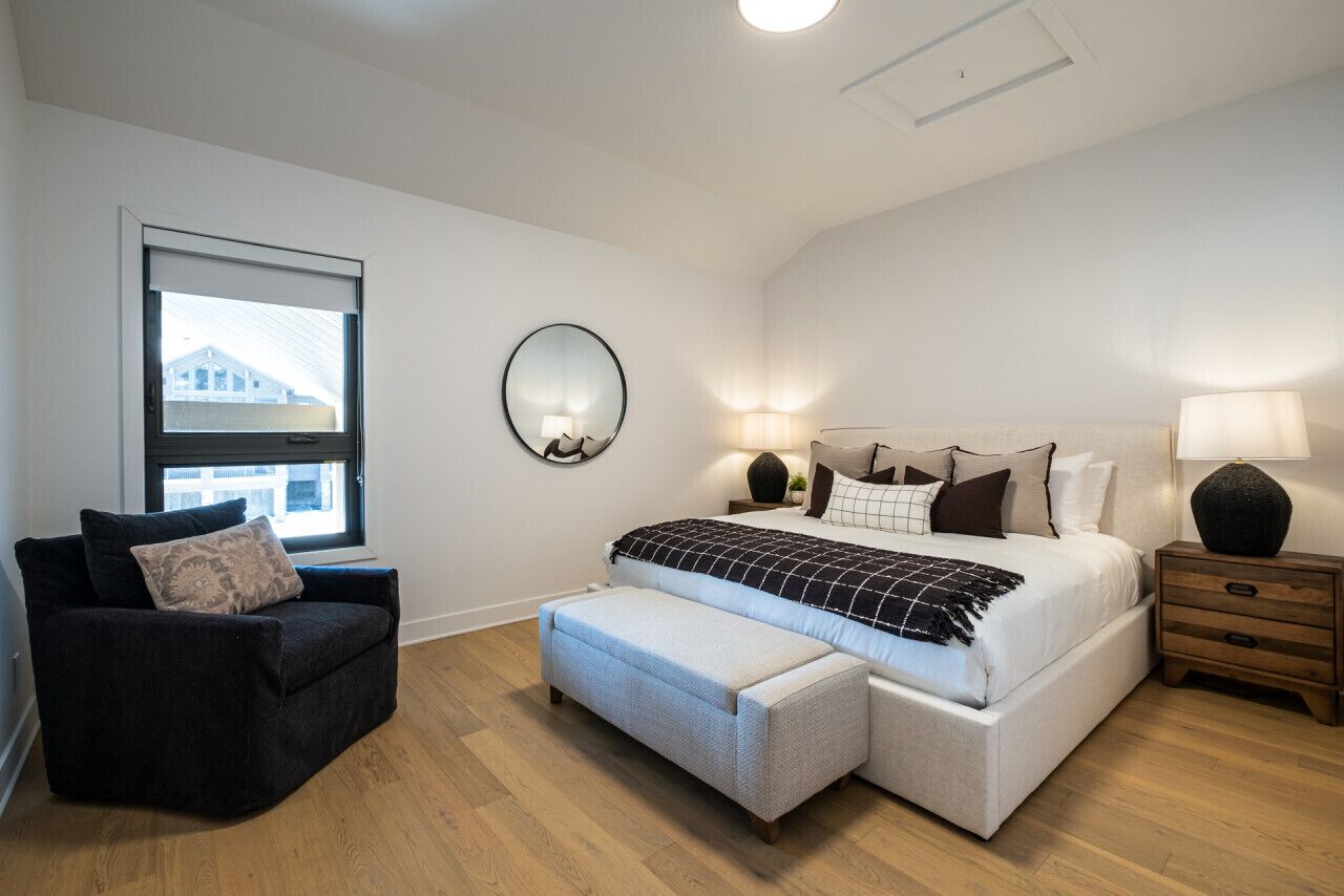 Une chambre à coucher comprenant un lit, des tables de chevet, une chaise, un banc, une fenêtre et un miroir.