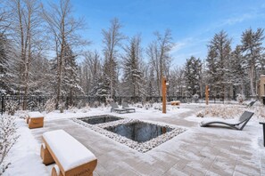 A snow-covered outdoor area with a pool, lounge chairs, and a wooden bench.