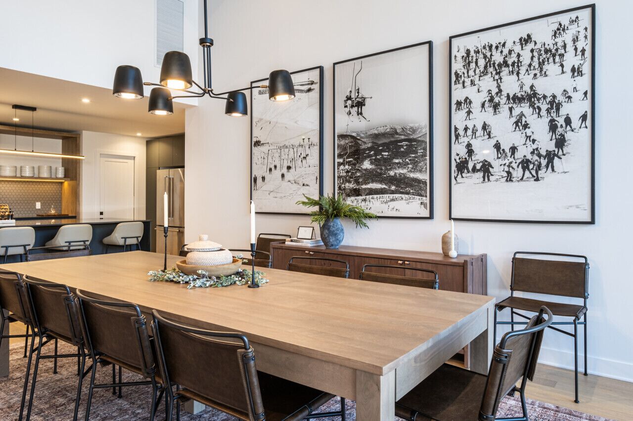 A modern dining area with a long wooden table, black chairs, and a chandelier.