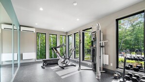 A modern gym with exercise equipment, large windows, and a view of greenery. - Tremblant Prestige - Verbier 12-101 (Mont-Tremblant)