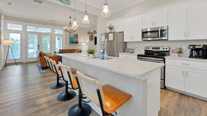 Une cuisine moderne avec des meubles blancs, des appareils en acier inoxydable et un îlot central doté de tabourets de bar.