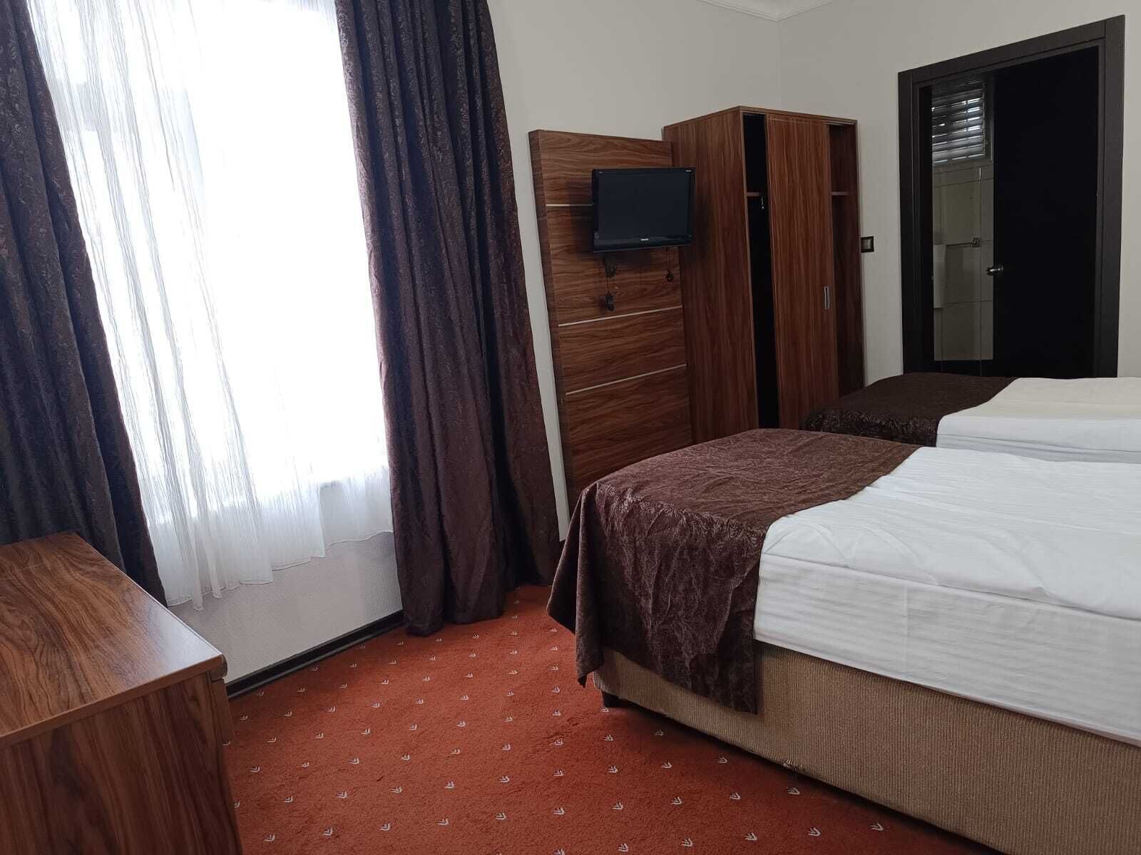 A hotel room with a bed, a wooden wardrobe, a television mounted on the wall, and a door with a mirror.