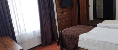 Habitación de hotel con cama, armario de madera, televisor montado en la pared y puerta con espejo.
