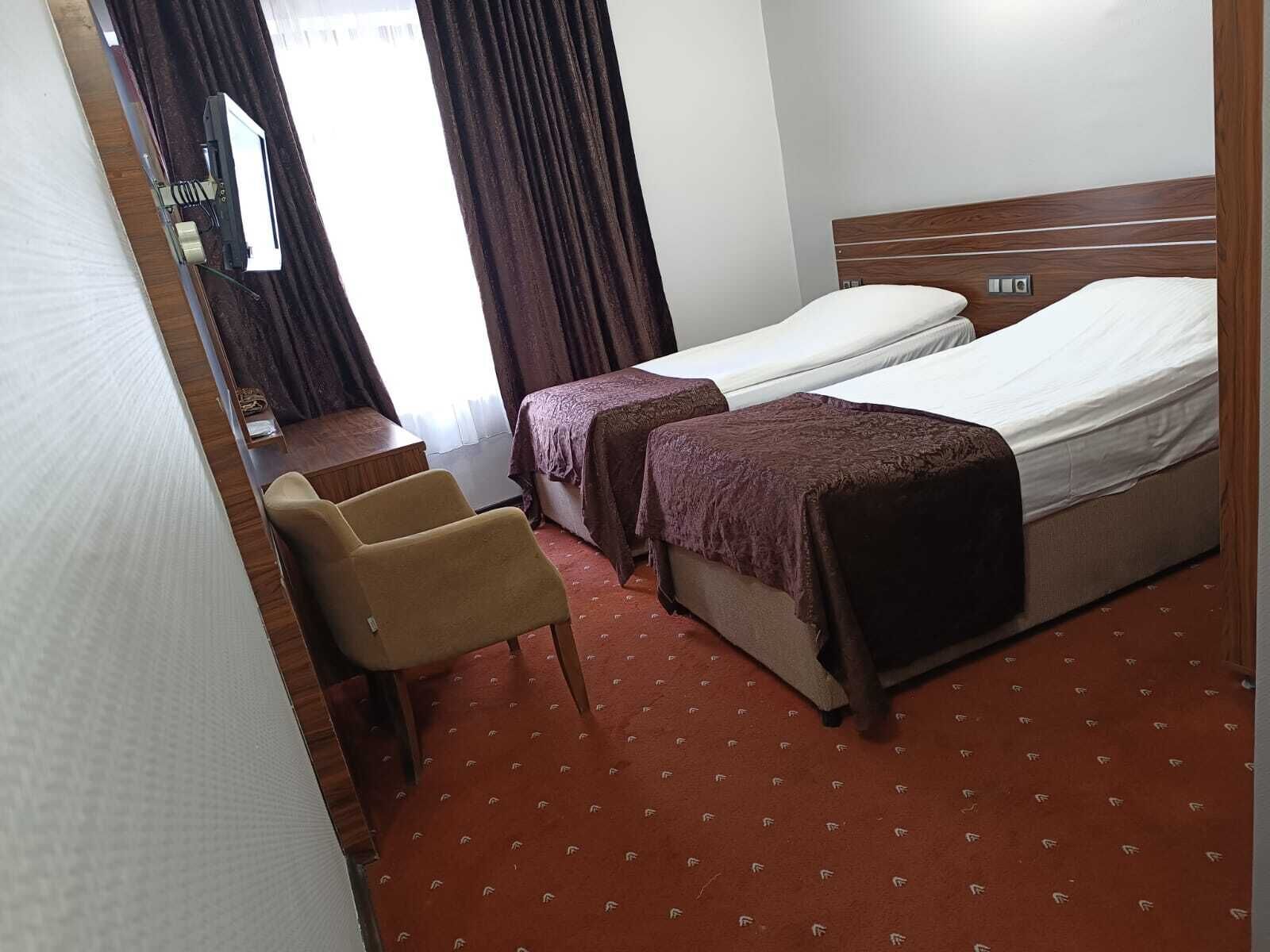 A hotel room with two beds, a desk, a chair, and a window with curtains.