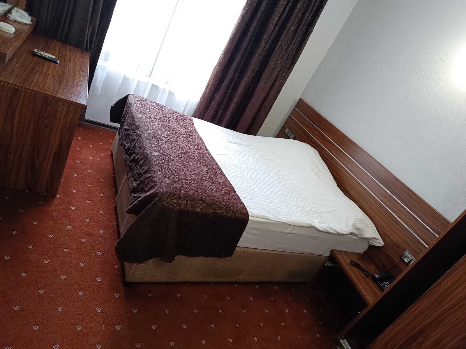 A compact hotel room with a single bed, a wooden desk, and a small bedside table.