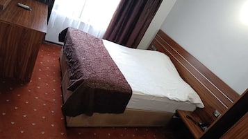 A compact hotel room with a single bed, a wooden desk, and a small bedside table.