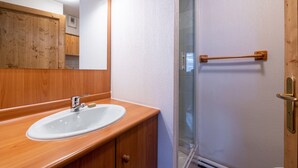 Un baño con tocador de madera, un lavabo blanco y una cabina de ducha de vidrio.