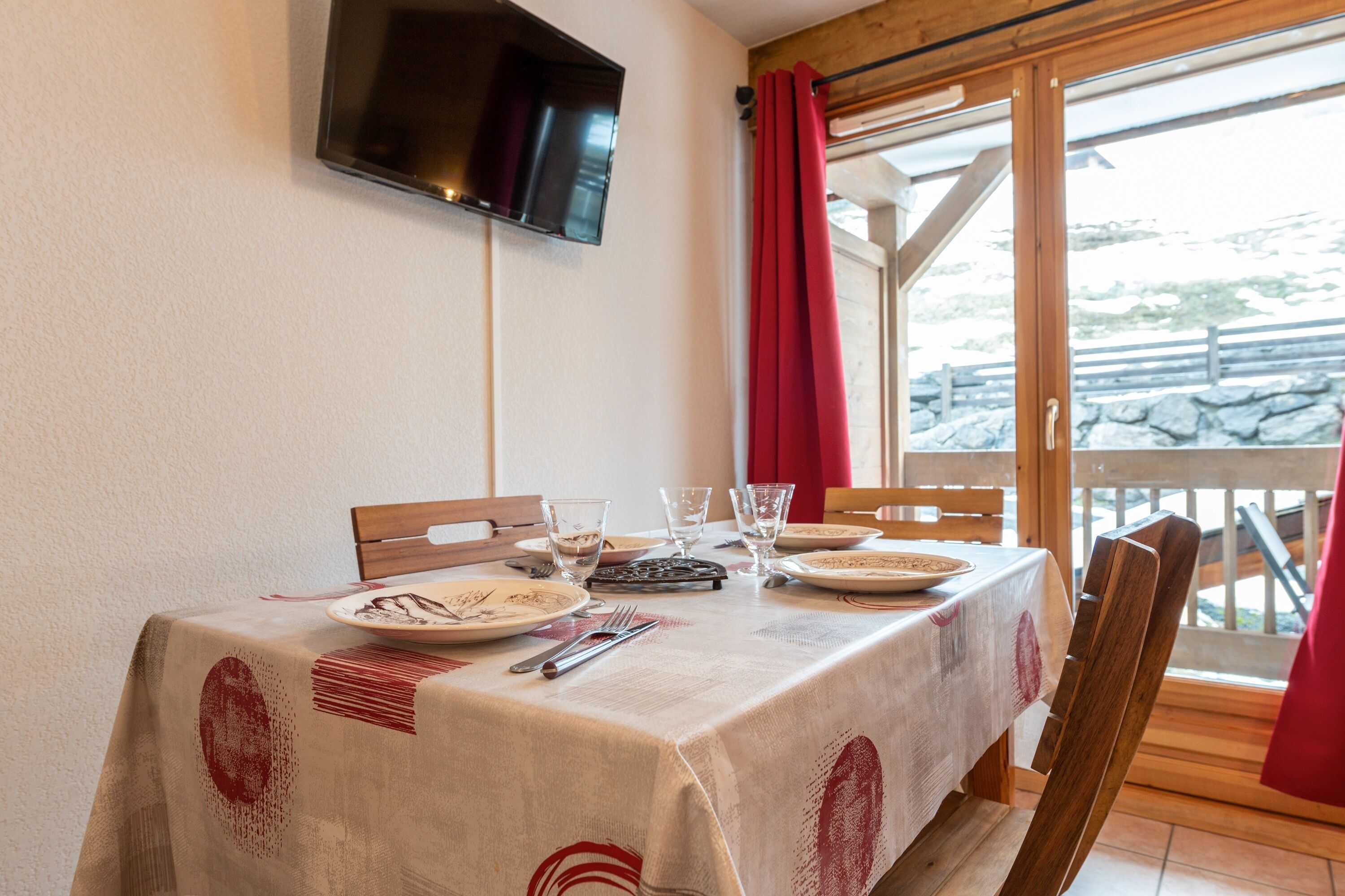 Een eettafel gedekt voor twee personen, met borden, bestek en glazen. Een televisie is aan de muur boven de tafel bevestigd.