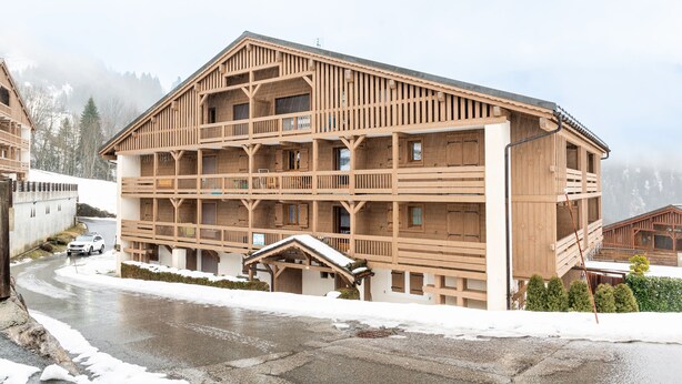 Un edificio de madera de varios pisos con balcones, una entrada cubierta y una calle nevada.