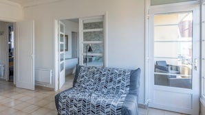 A modern living room with a patterned sofa, a glass door leading to an outdoor area, and a view of the cityscape. - Mélodie - Bel appartement vue mer (Criel-sur-Mer)