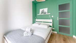 A bedroom with a bed, white headboard, and a green wall. There is a door with frosted glass panels and a white towel on the bed. - Le Rex - Bel appt avec sauna (Nantes)