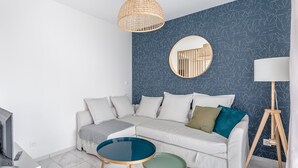 A modern living room with a sectional sofa, a round mirror, a small round table, and a floor lamp. - Le Rex - Bel appt avec sauna (Nantes)