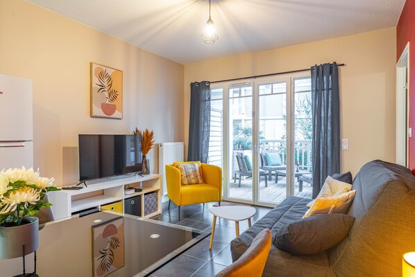 A modern living room with a flat-screen TV, a sofa, a yellow armchair, and a dining area with a table and chairs.