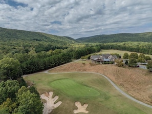 Um campo de golfe com uma casa e floresta circundante.