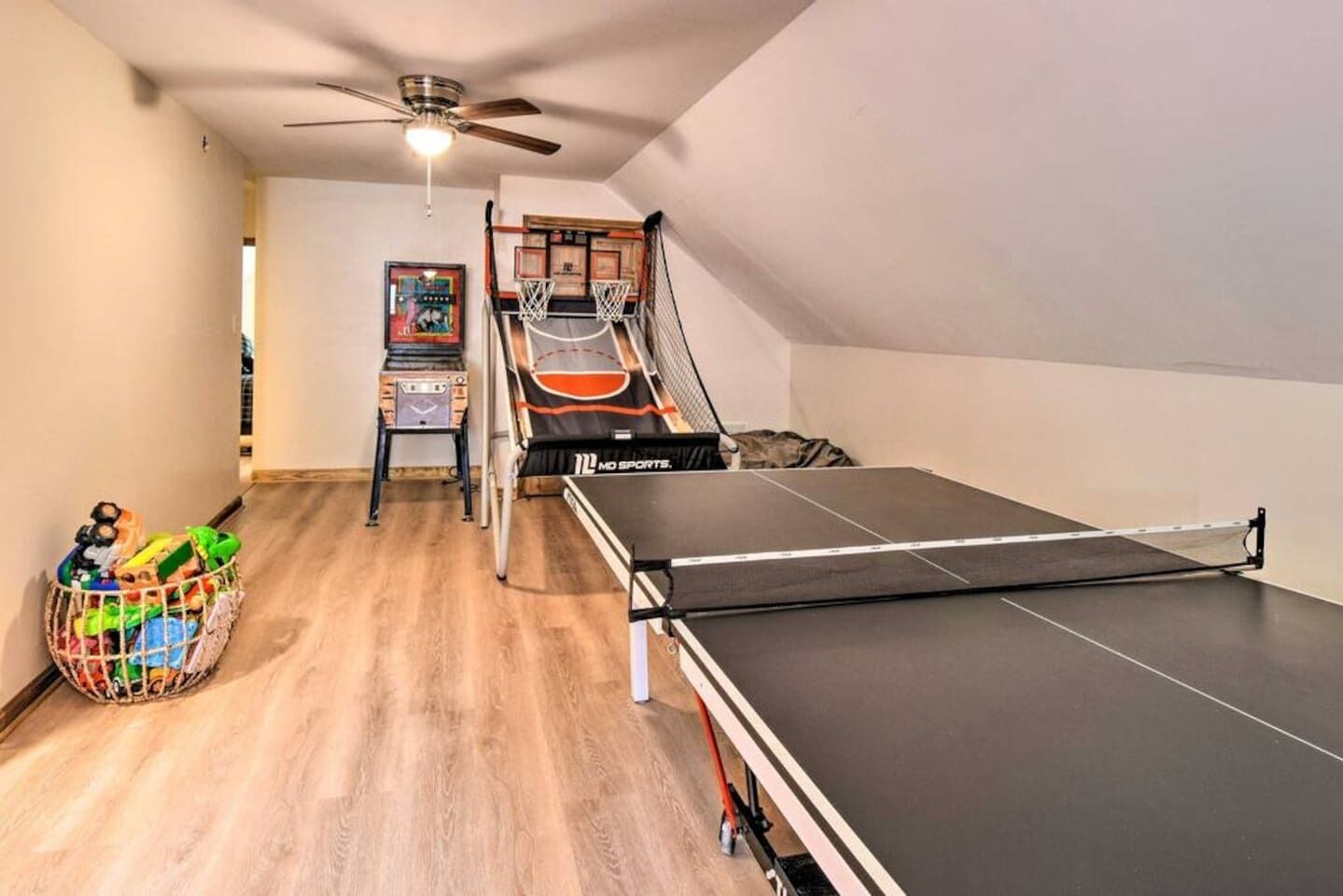 A room with a ping pong table, a ceiling fan, a basketball hoop, and a small basketball court.