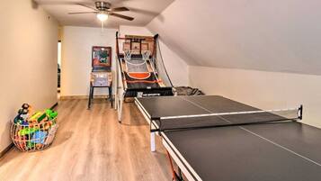A room with a ping pong table, a ceiling fan, a basketball hoop, and a small basketball court.
