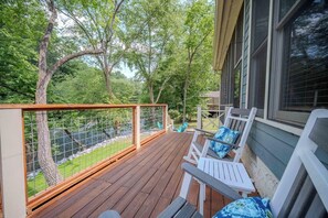 A wooden deck with a railing, white rocking chairs, and a view of a river and trees. - Ellijay | Screened Porch | River Access | Gameroom (Ellijay)