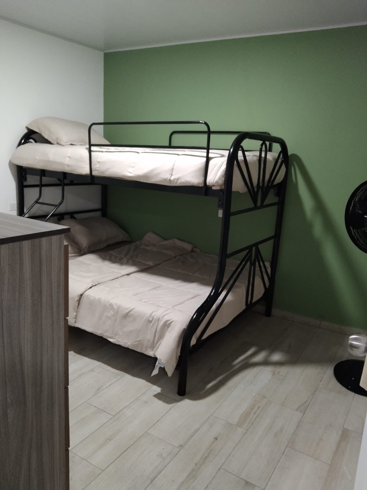 Une chambre avec un lit superposé, un bureau et un ventilateur.