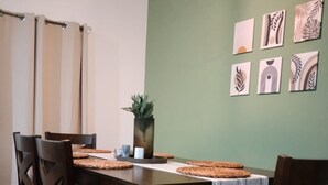 Comedor con mesa de madera, cuatro sillas y una pared verde decorada con cuadros.