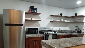 Una cocina moderna con electrodomésticos de acero inoxidable, encimeras de granito, armarios de madera y estantes integrados.
