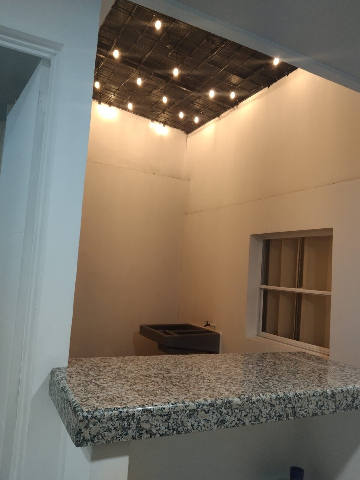 A bathroom with a granite countertop, a window, and a ceiling with exposed beams and lights.
