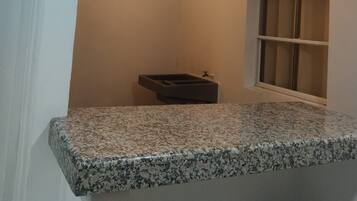 A bathroom with a granite countertop, a window, and a ceiling with exposed beams and lights.