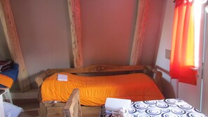 A small, cozy room with a single bed, a wooden headboard, and a window with red curtains. - Complejo de Cabañas Tierra de Luna  (Potrerillos)