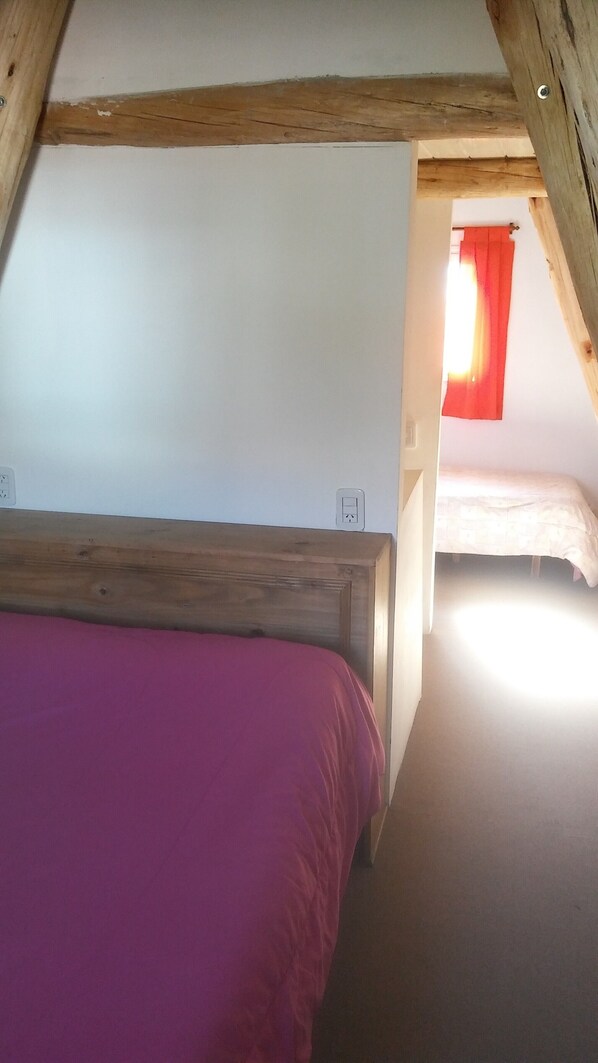 A bedroom with a wooden ceiling, a bed with a purple bedspread, and a window with a red curtain.