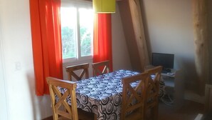 Un comedor con una mesa y sillas, una ventana con cortinas rojas y un televisor sobre un mueble.