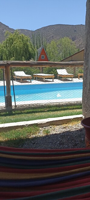 A pool area with lounge chairs and a red building in the background. - Complejo de Cabañas Tierra de Luna  (Potrerillos)