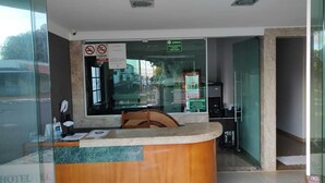 A hotel reception area with a wooden reception desk, a glass partition, and a Coca-Cola advertisement on the window.