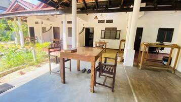 Une pièce spacieuse avec une table et des chaises en bois, un ventilateur de plafond et une vue sur un jardin.