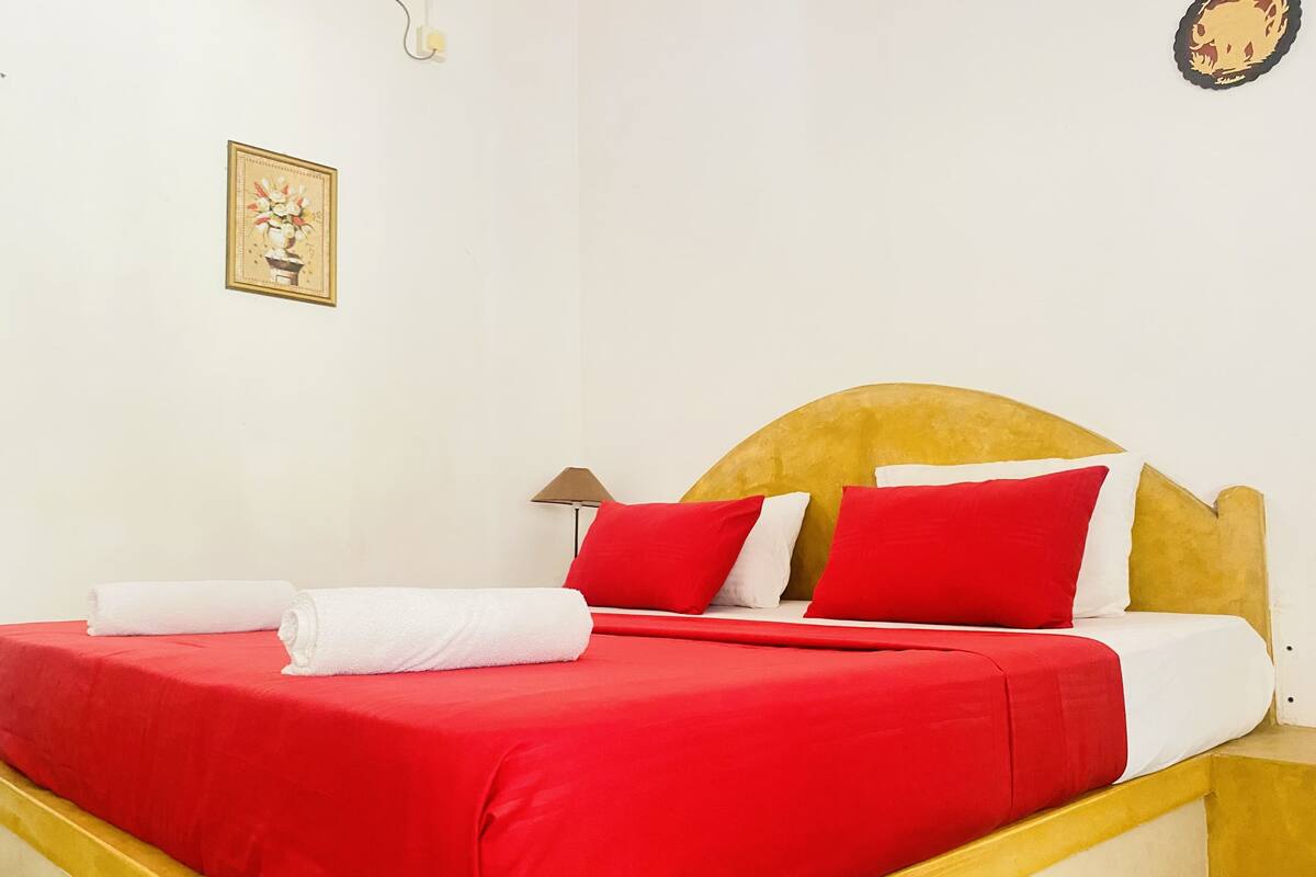 Ein Bett mit rot-weiß gestreifter Bettwäsche, einem hölzernen Kopfteil und einer kleinen Nachttischlampe.