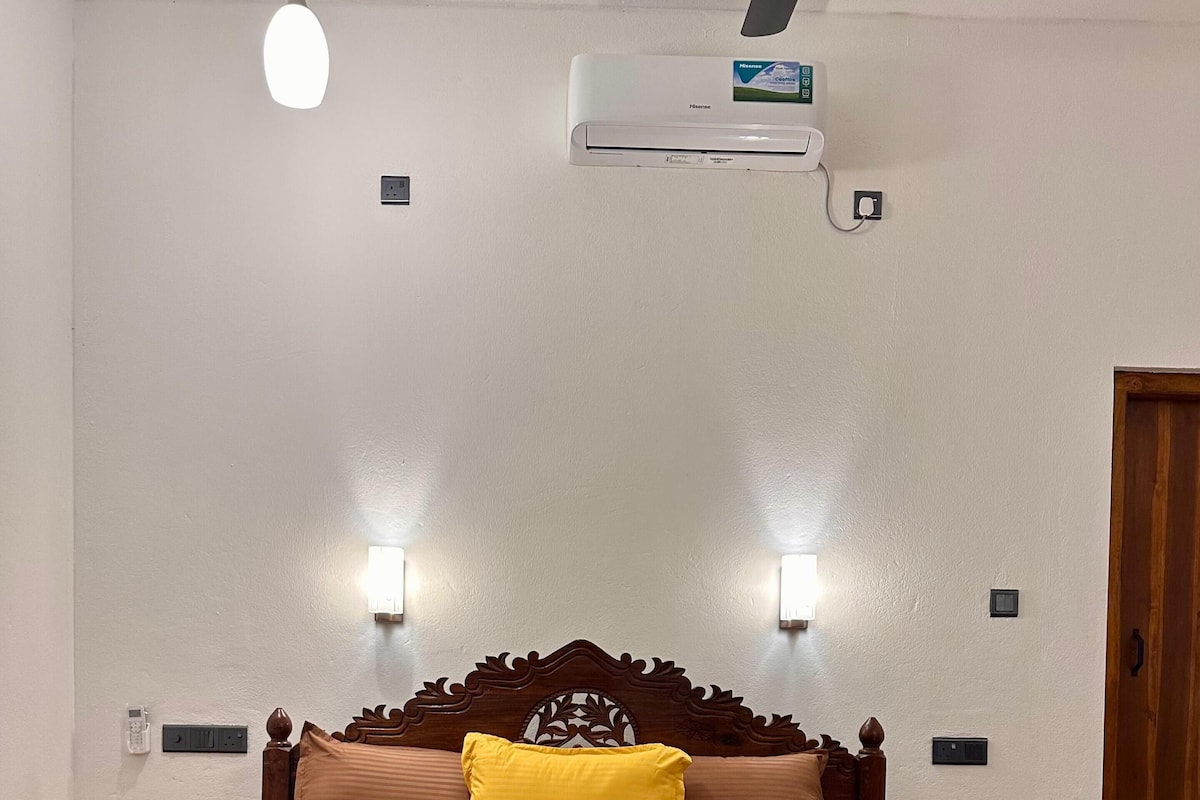 Ein Bett mit Holz-Kopfteil, zwei Nachttischlampen und einer Wand-Klimaanlage.