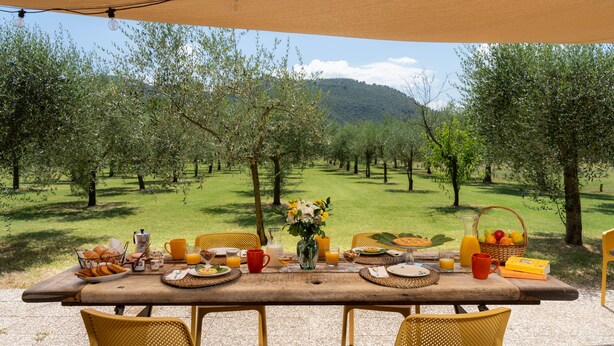 A table set outdoors with breakfast items, surrounded by chairs, and overlooking a lush orchard. - A typical Italian Villa in the center of Italy.  (spoleto)